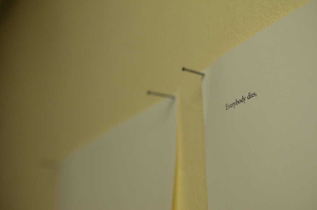 two sheets of a4 paper hang are pinned to a wall. Each sheet has a single line of typewritten text on it. In the bottom right hand corner of the left sheet, is written the line 'And he was dead.' full stop. In the top left hand corner of the right sheet, is written the line 'Everybody dies,' comma.