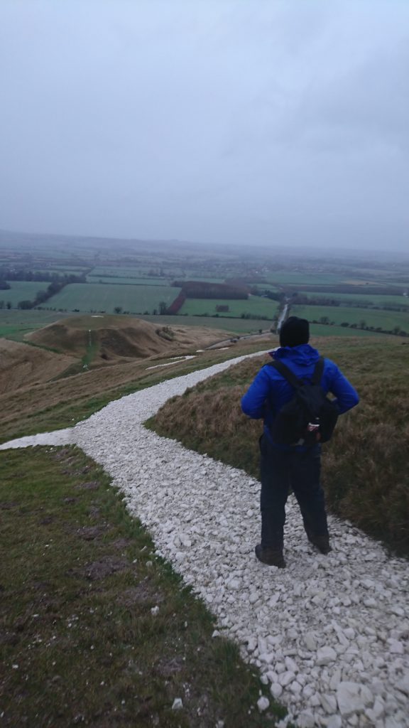 A man pictured from behind stands on a white chalk path, looking out over a misty landscape.